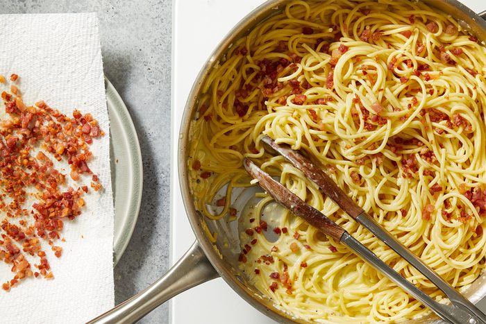 Overhead shot of spaghetti tossed with egg and cheese mixture in the pan, forming a glossy carbonara sauce.