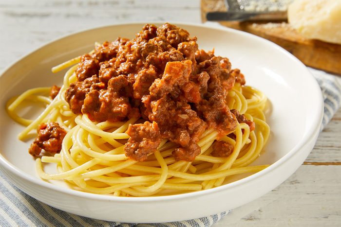 Close up shot of a bowl of spaghetti generously topped with Slow-Cooker Bolognese, highlighting the chunky meat sauce over pasta.