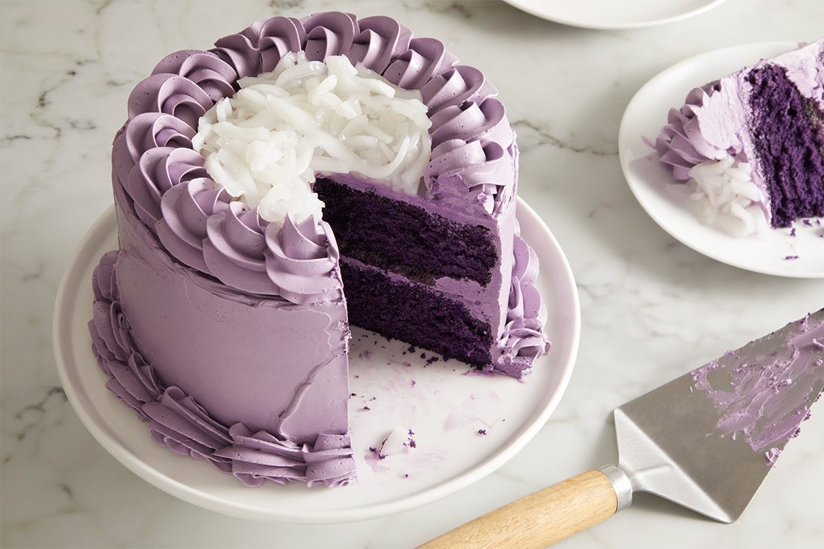 3/4 shot of the finished Ube Cake with a large slice removed, revealing the deep purple interior and fluffy texture, placed beside a cake server on the table.