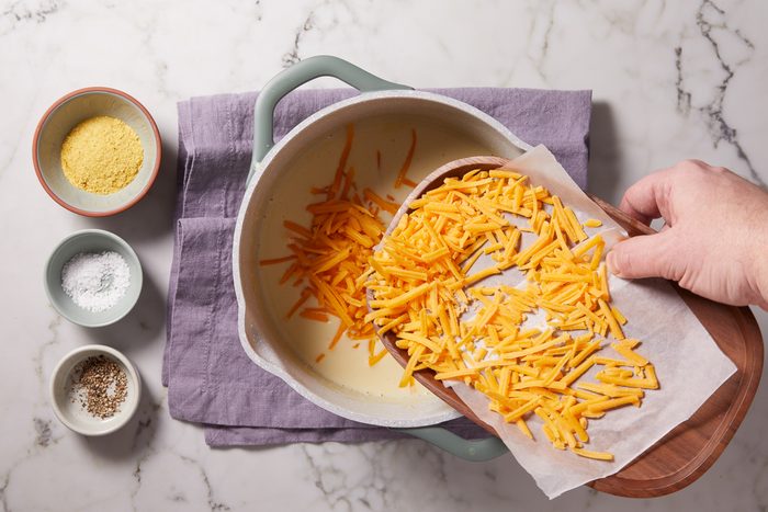 shredded cheese being added to sauce mixture