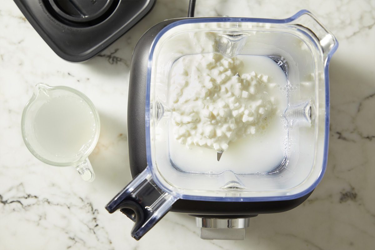 Cottage cheese shown in a blender with liquid, prepared for blending until smooth. This step creates a lighter, protein-rich alternative to heavy cream for the vodka sauce.