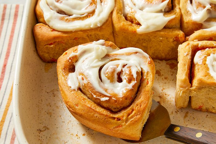 Overhead close-up of finished carrot cake cinnamon rolls generously topped with cream cheese frosting.