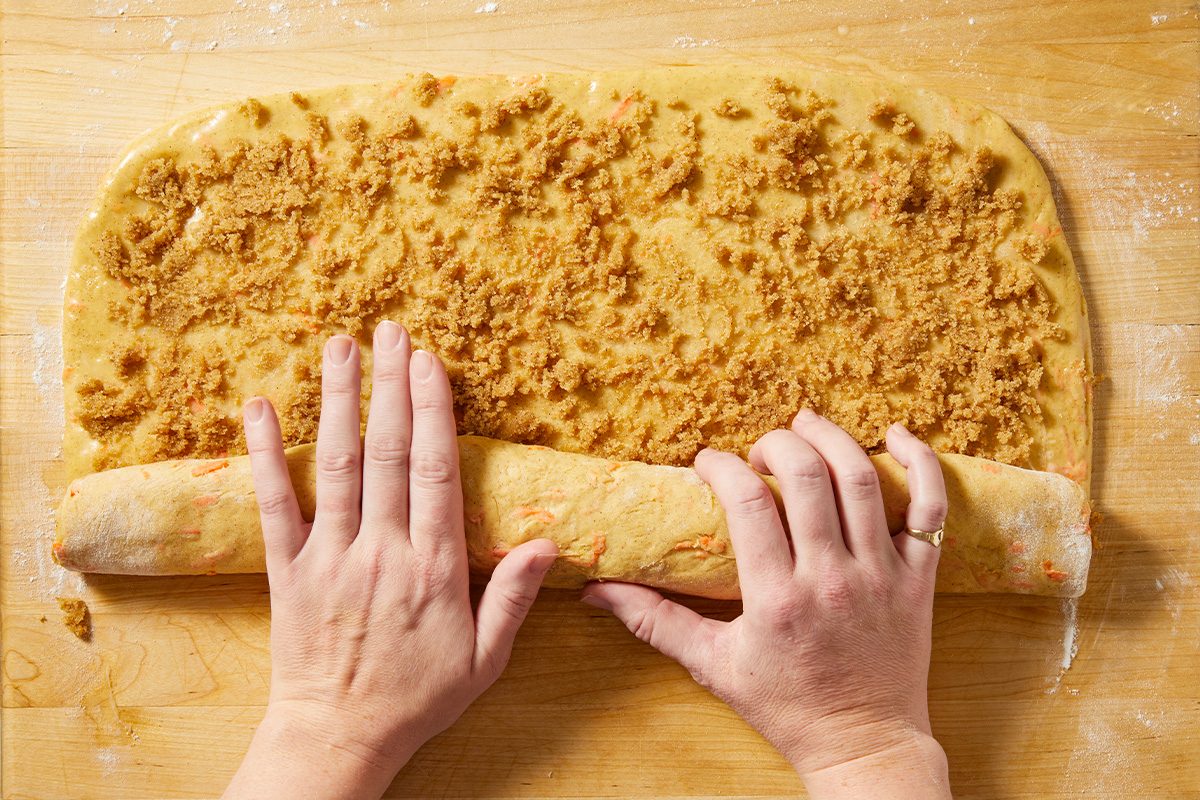 Overhead view of cinnamon sugar filling being spread evenly over rolled carrot cake dough.