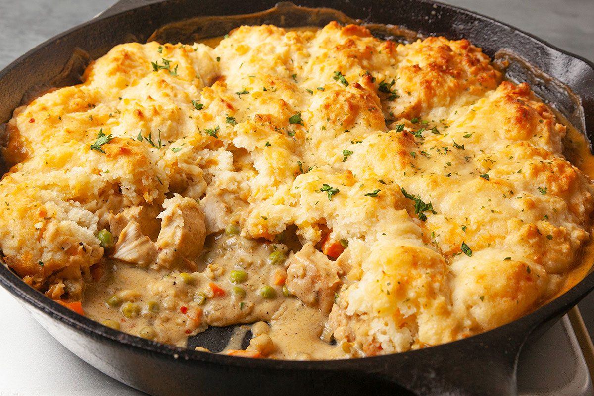 Overhead horizontal image of a fully baked Cheddar Bay Chicken Pot Pie in a cast iron skillet, featuring a golden, flaky Cheddar Bay biscuit topping with visible herbs and browned texture. This final hero shot highlights the completed comfort food dish with a rustic, homemade presentation.