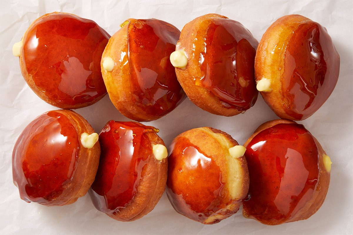 A horizontal overhead image featuring a neat row of Crème Brûlée Doughnuts with shiny caramelized sugar tops. The image emphasizes uniformity and texture of the finished dessert.