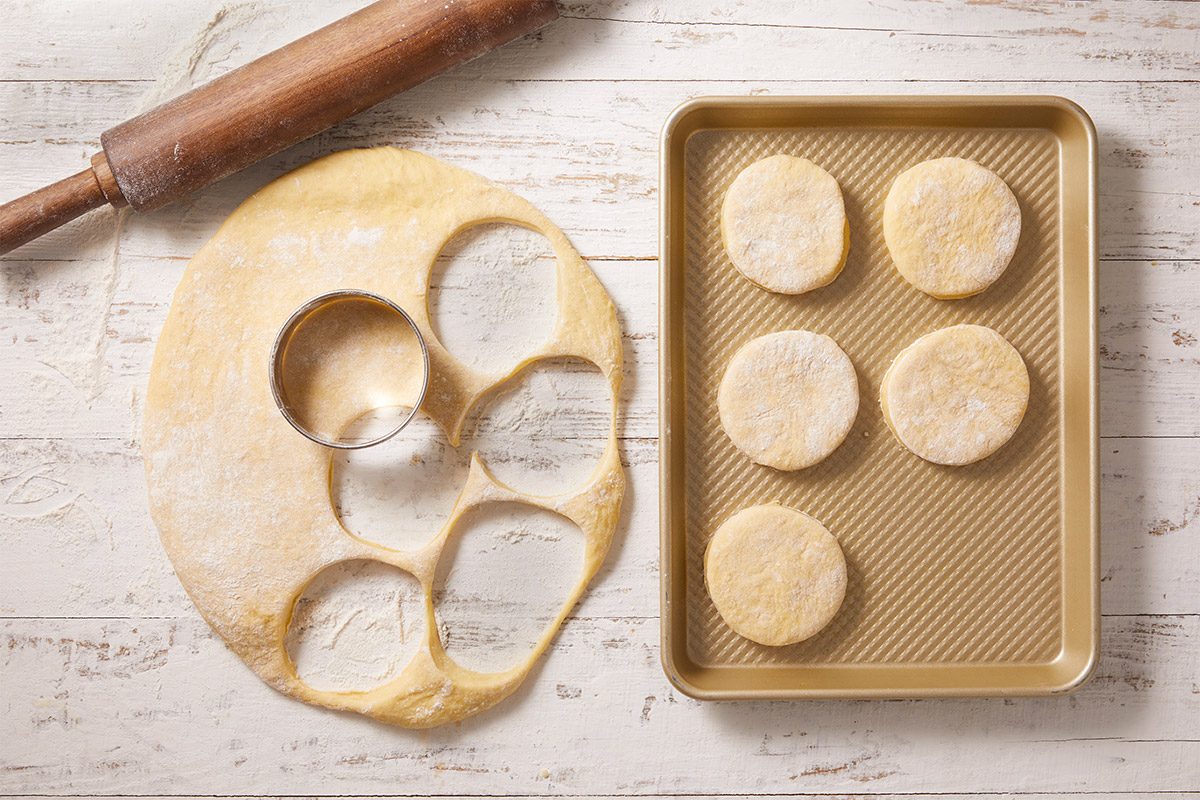An overhead, horizontal image showing cut rounds of dough arranged on a baking sheet before frying. This step highlights shaping dough for Crème Brûlée Doughnuts.