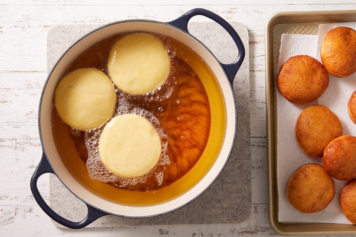An overhead, horizontal step-by-step image showing doughnuts frying in hot oil inside a deep pot. The doughnuts are turning golden brown as part of the Crème Brûlée Doughnuts preparation.