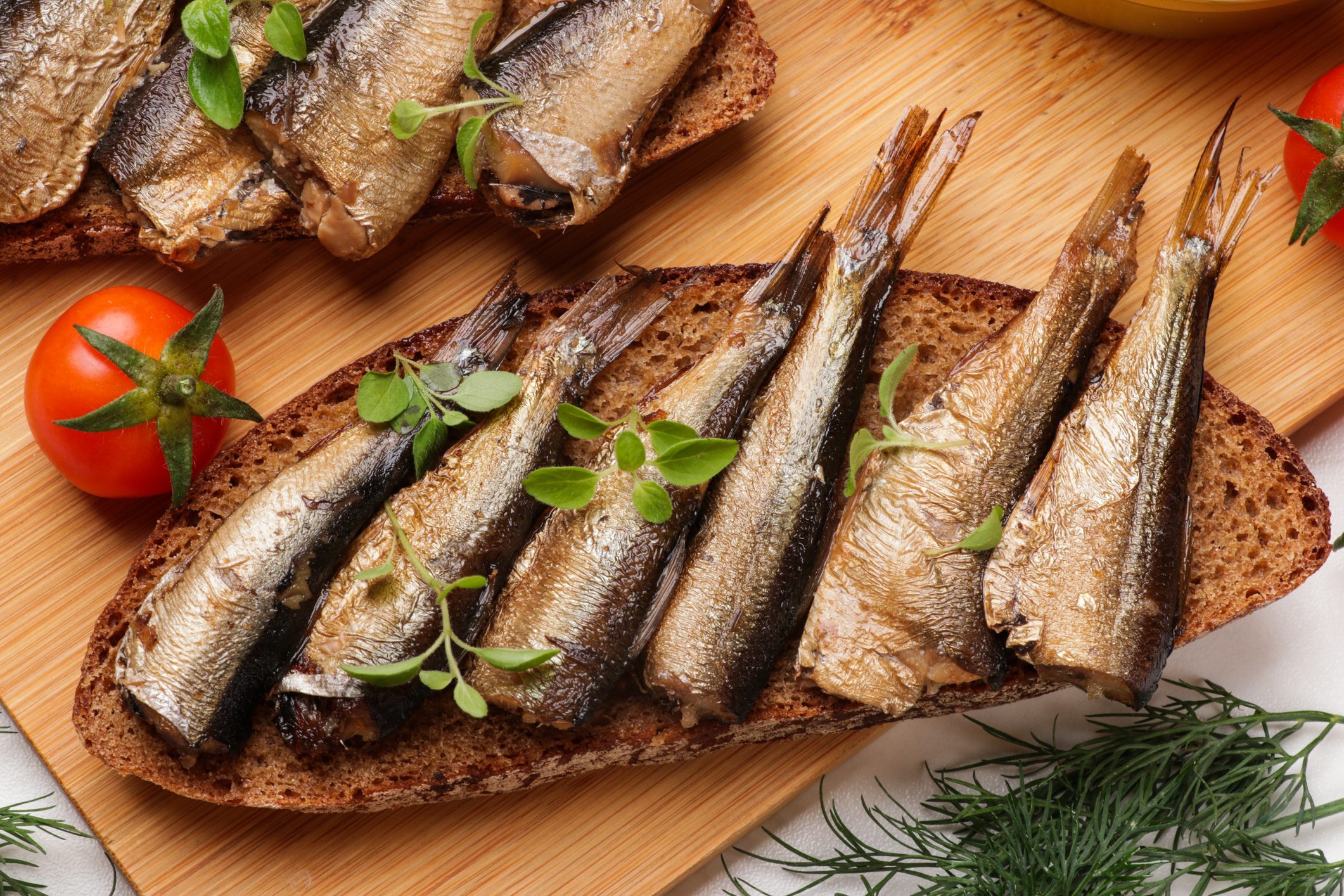 Delicious sandwiches with sprats, microgreens and dill on white table, top view