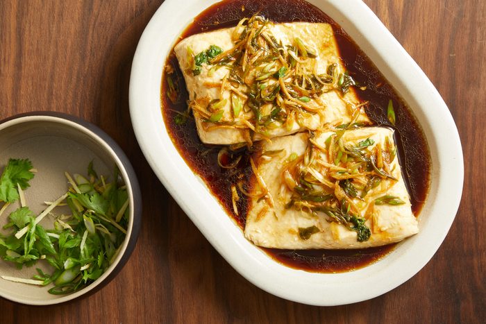 hot sauce poured over fish with ginger, scallion and cilantro mixture in a bowl next to it