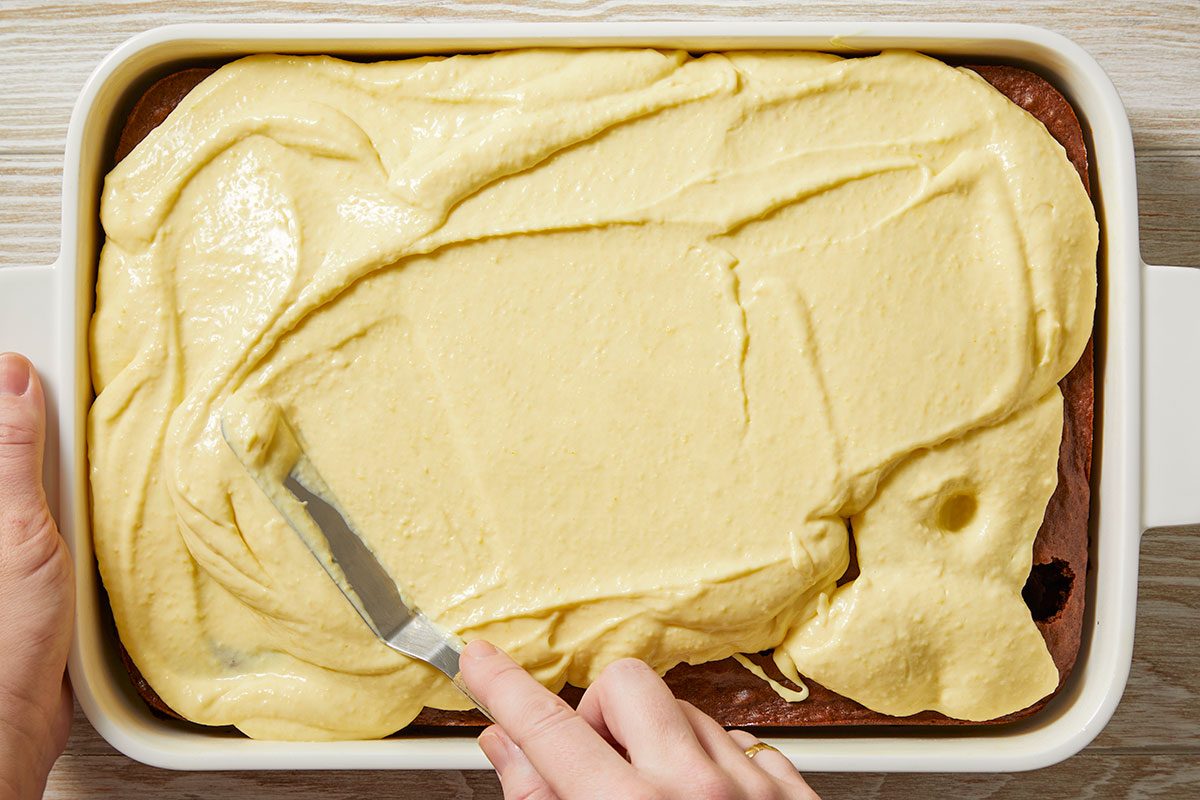 Overhead view of the Irish cream filling spread evenly across the surface of the baked chocolate cake, allowing the mixture to soak into the holes.