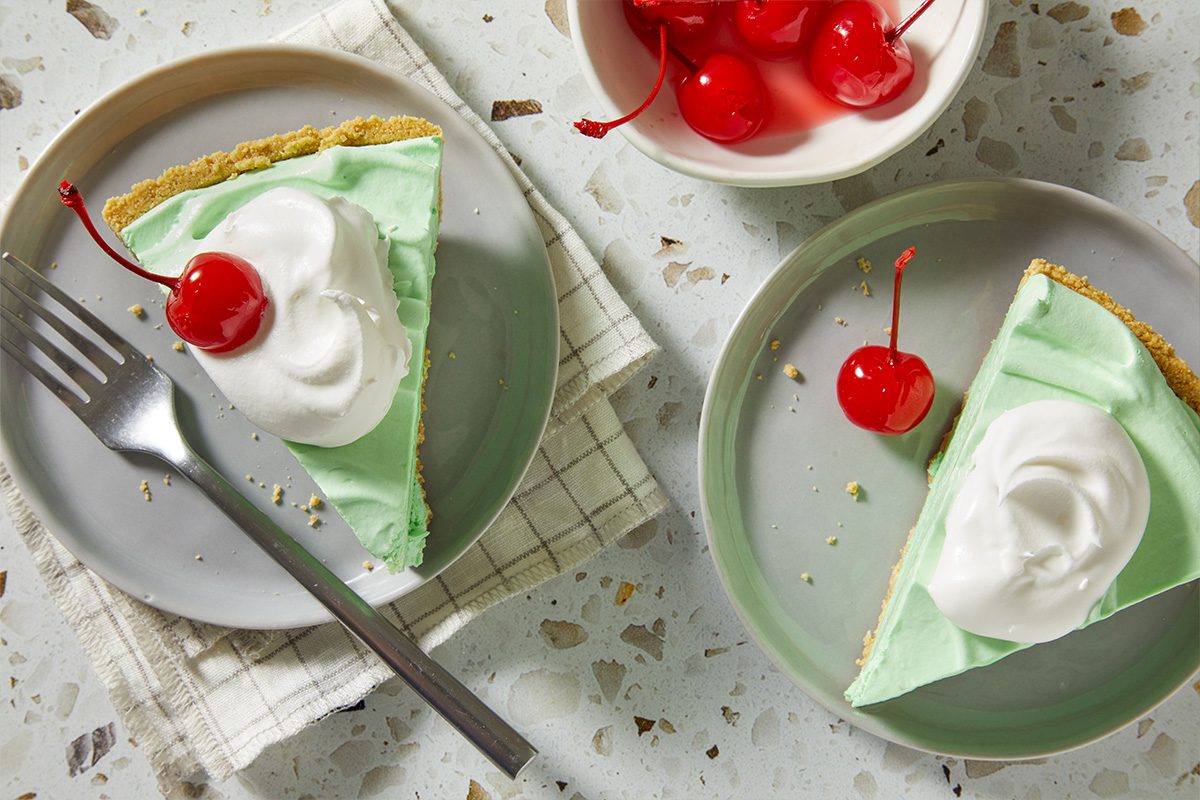 Overhead, horizontal image of a finished Shamrock Shake Pie slice served alongside additional garnishes and tableware. The final presentation emphasizes readiness to serve and celebratory appeal.