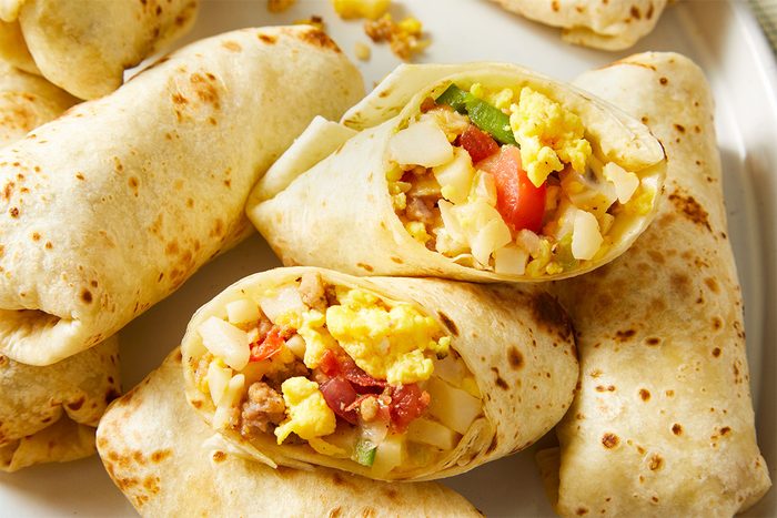 Close up shot of Slow-Cooker Breakfast Burritos loosely folded and displayed on a plate for easy grabbing.