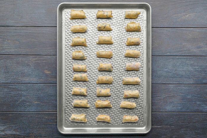 A baking sheet with neatly arranged, evenly spaced, uncooked stuffed pasta pieces on a textured metal tray, placed on a dark wooden surface.